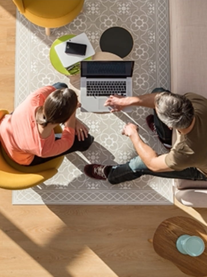 Vista de cima de um casal sentado no chão usando um laptop acessando o site de Portinari.