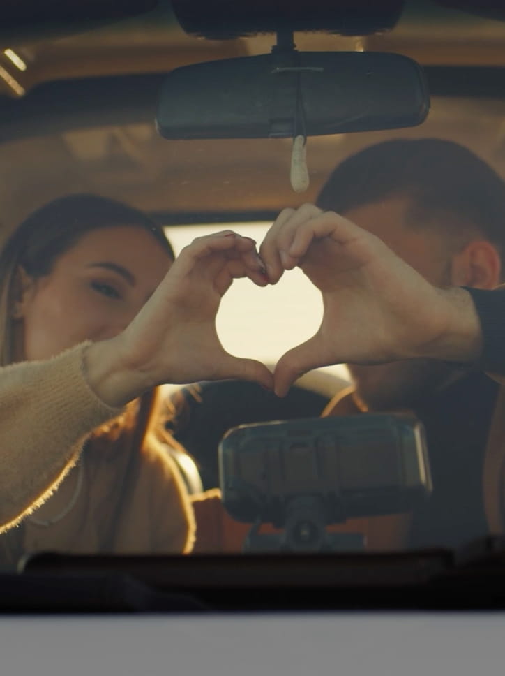 Cena de um casal dentro de um carro, formando um coração com as mãos na campanha de MILITEC 1.