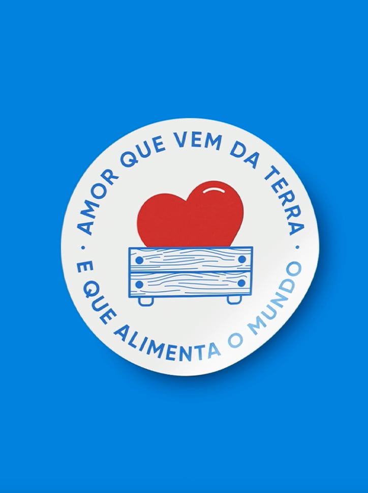 Selo da campanha "Amor que vem da terra e que alimenta o mundo", com uma arte circular que mostra um coração dentro de um caixote de madeira.