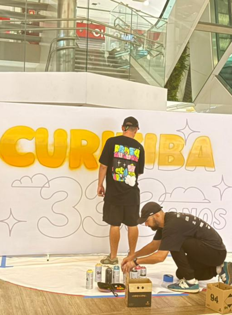 Diego Prosa pinta o mural “Curitiba 333 anos” durante a fase de preparação da intervenção artística no Shopping Mueller, ajustando detalhes da obra que será finalizada de forma colaborativa com a participação do público.